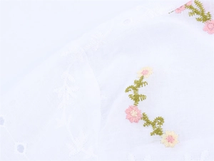 Gros plan sur tissu en coton blanc avec broderies florales et détails ajourés délicats