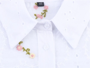 Détail de chemise blanche en coton brodé avec fleurs et étiquette de taille XS