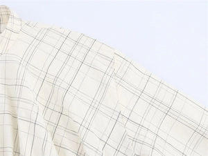 Close-up detail of beige plaid fabric texture on long sleeve bomber style shirt jacket