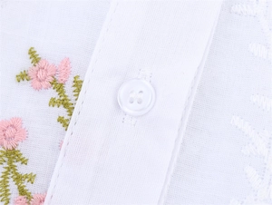 Détail d'une chemise en coton blanc avec broderie florale délicate et bouton blanc