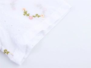 Détail du tissu en coton blanc avec broderie anglaise et motifs floraux aux poignets