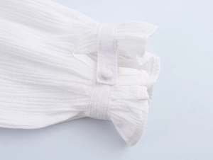 Dettaglio del polsino bianco con cinturino a bottone e trame di ricamo a balze eleganti