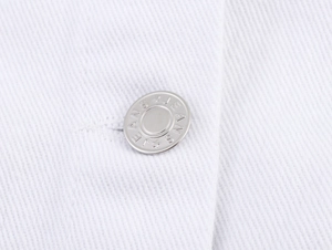 Makroaufnahme eines silbernen Jeansknopfes auf weißem Twillstoff-Detail der Kleidung