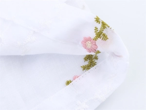Détail de broderie florale raffinée sur un tissu de chemise d'été en coton blanc