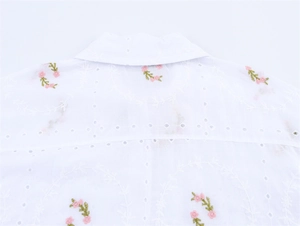 Détail de chemise blanche en coton avec broderie florale rose et finitions délicates du col