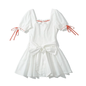 Détail de la robe en coton brodé blanc avec nœuds en ruban rouge et encolure carrée