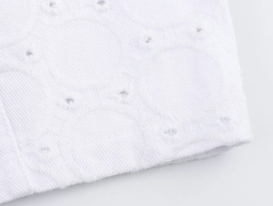 Nahaufnahme von weißem Baumwollstoff mit geometrischer Stickerei und hohlen Details am Saum
