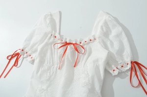 Détail de la robe en dentelle blanche avec nœuds rouges et broderies florales fines