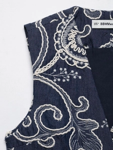 Detailed close-up of intricate white floral embroidery on a navy denim vest with V-neckline