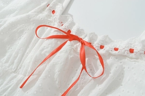 Détail d'une robe blanche en broderie anglaise avec encolure élastique et nœud en satin rouge