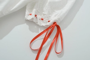 Détail d'une robe en broderie anglaise blanche avec un ruban de satin rouge contrasté