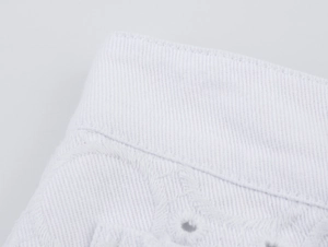 Makro-Detail von weißem Twill-Stoff mit filigraner Eyelet-Stickerei und feiner Schnittführung