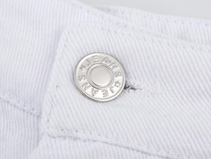 Detailaufnahme eines silbernen Metallknopfs auf weißen Denim-Shorts mit sauberer Naht