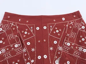 Détail d'une jupe rouge bohème avec broderie géométrique et paillettes miroir fines