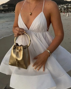 Dettaglio di un abito bianco con profondo scollo a V e una borsa a secchiello dorata