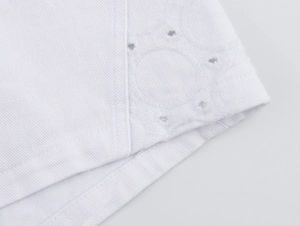 Detail eines weißen Baumwoll-Sets mit zarter Ösenstickerei und Hohlstickerei am Saum