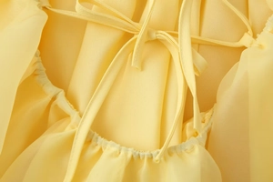 Dettaglio di un abito in chiffon giallo chiaro con lacci sulla schiena e bordi arricciati