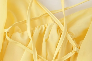 Dettaglio dell'abito giallo chiaro con spalline incrociate e trama del tessuto arricciato