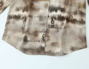 Detail of earthy tie-dye pattern on smooth long-sleeved shirt with small buttons