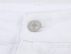 Makroaufnahme eines silbernen Metallknopfs mit JEANS-Gravur am weißen Denim-Bund