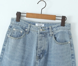 Detail view of light blue denim jeans waist with metal button and woven brand label