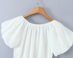 Détail d'un haut blanc à manches bouffantes et col bardot élastique sur un cintre