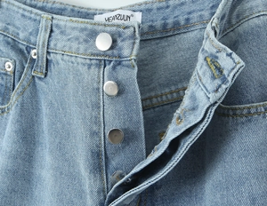 Detail of light blue denim jeans showing button fly closure and woven waist label