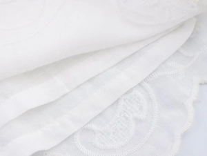 Close-up of elegant white eyelet embroidery and scalloped edge detail on lightweight fabric