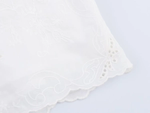Detail of white scalloped hem with delicate floral embroidery and cut-out lace details