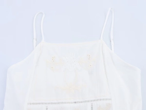 Detail of white camisole top featuring delicate flower embroidery and lace trim edges