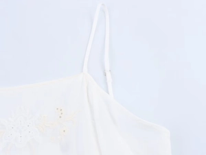 Close-up of delicate floral embroidery and adjustable spaghetti straps on white camisole top