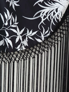 Détail de la broderie de feuilles blanches et des longues franges noires sur la robe