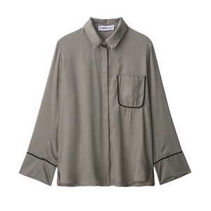 Close-up of olive green long sleeve shirt featuring black piping and chest pocket detail