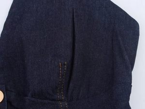 Detailed close-up of dark blue denim fabric with orange contrast stitching and metal rivet