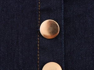 Detailed macro view of dark blue denim fabric with contrast stitching and metal button