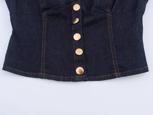 Detail of dark blue denim corset top featuring five gold metal buttons and orange stitching
