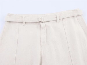 Detail of cream high-waisted cotton pants with matching belt and silver D-ring buckle
