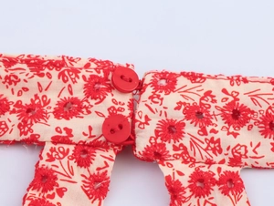 Detail of red floral embroidery and two matching buttons on white eyelet fabric