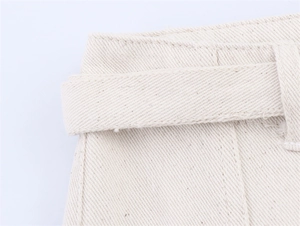 Detail shot of the belt loops and twill fabric texture on cream denim shorts