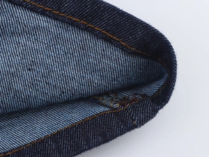 Macro detail of dark blue denim fabric with precise orange contrast stitching and texture