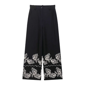 Detailed view of white paisley embroidery on high-waist black wide-leg trousers