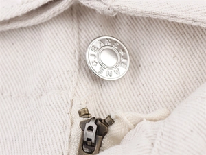 Detailed close-up of engraved metal button and zipper on cream denim vest set