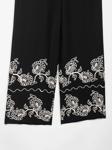 Detailed embroidery on the hem of black wide-leg trousers with floral paisley patterns
