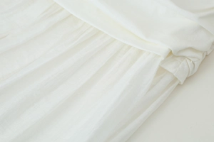 Détail de la robe midi blanche montrant les plis délicats et la taille froncée artisanale