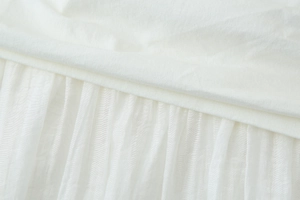 Détail macro d'une robe midi blanche montrant des plis délicats et le patchwork