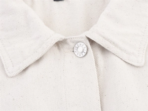Close-up of oatmeal denim jacket collar with detailed metal button featuring JEANS text