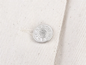 Macro shot of silver embossed jeans button on premium off-white heavy twill denim fabric