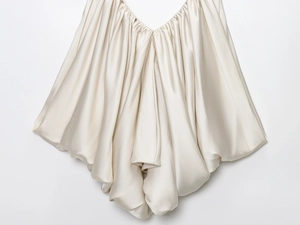 Detailed view of champagne satin fabric with elegant pleated textures and glossy finish