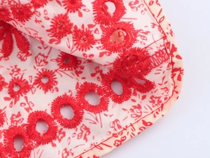 Detail view of white cotton fabric with red floral embroidery and eyelet hollow cutouts