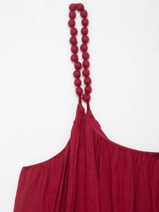 Détail de la bretelle de robe rouge foncé avec perles en tissu et texture plissée